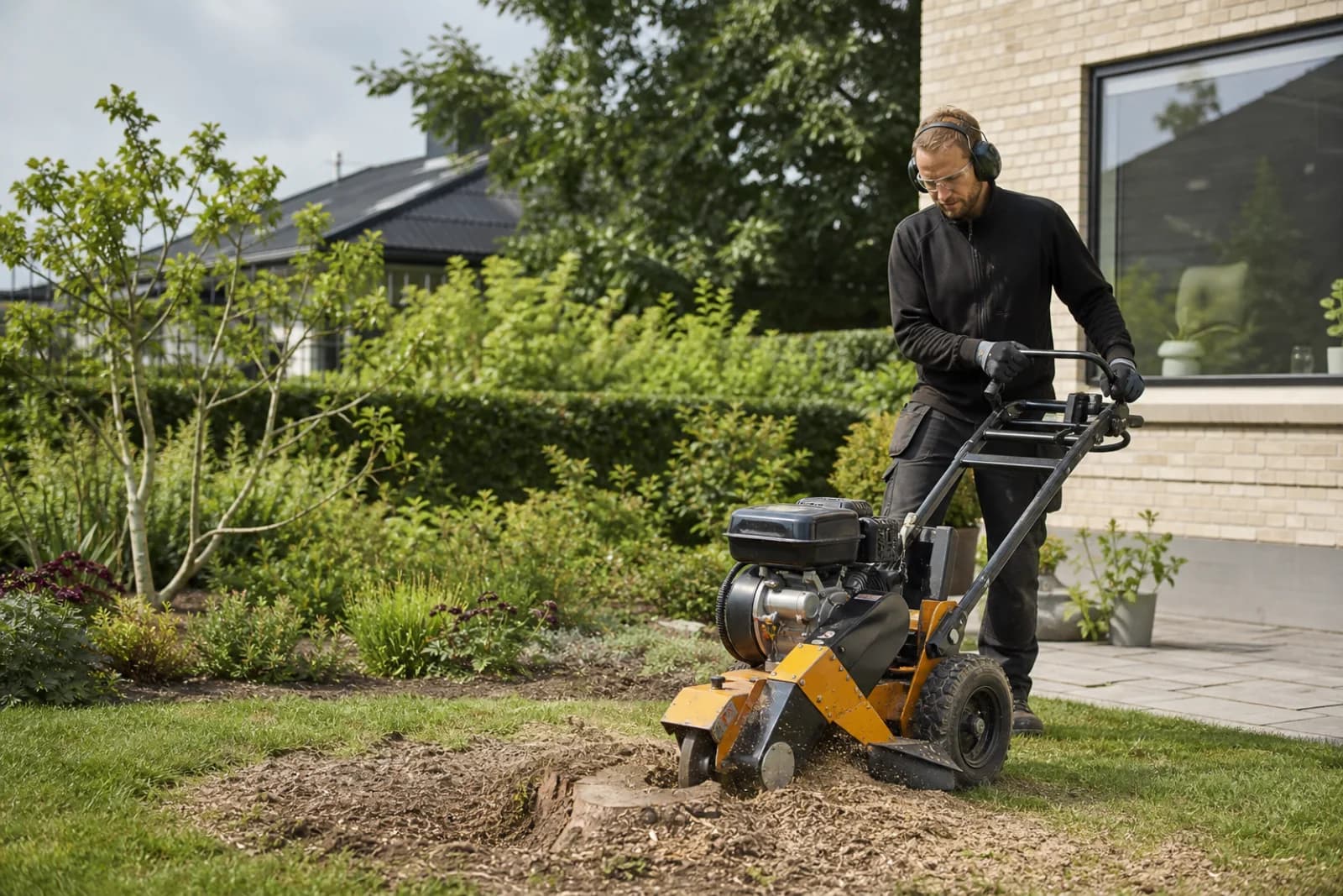 Fagperson fræser en træstub i en dansk villahave